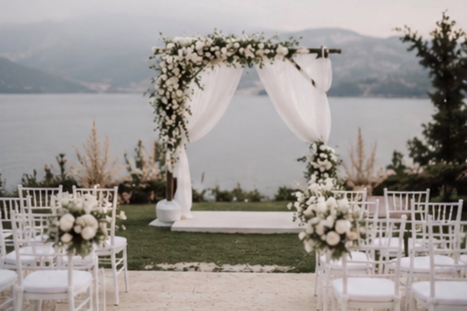 Elegant outdoor wedding ceremony setup with floral arch and chairs by the water.